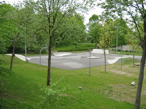 Bild vom Skatepark Ahrensbök. Zu sehen ist eine Grünfläche mit Bäumen. Dahinter befinden sich mehrere Rampen. 