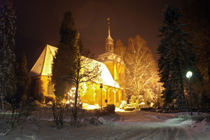 Bild der evangelischen lutherischen Kirche im Winter. Um die Kirche herum liegt Schnee und diese wird durch Strahler beleuchtet.