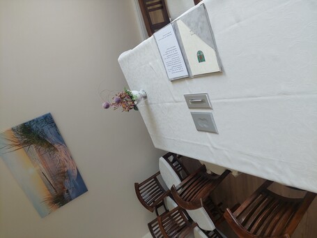Bild vom Trauzimmer im Bürgerhaus mit braunen Stühlen und einem Tisch mit heller Tischdecke auf dem ein Ordner liegt und eine Blume steht. An der Wand hängt ein Strandbild vom Sonnenuntergang.